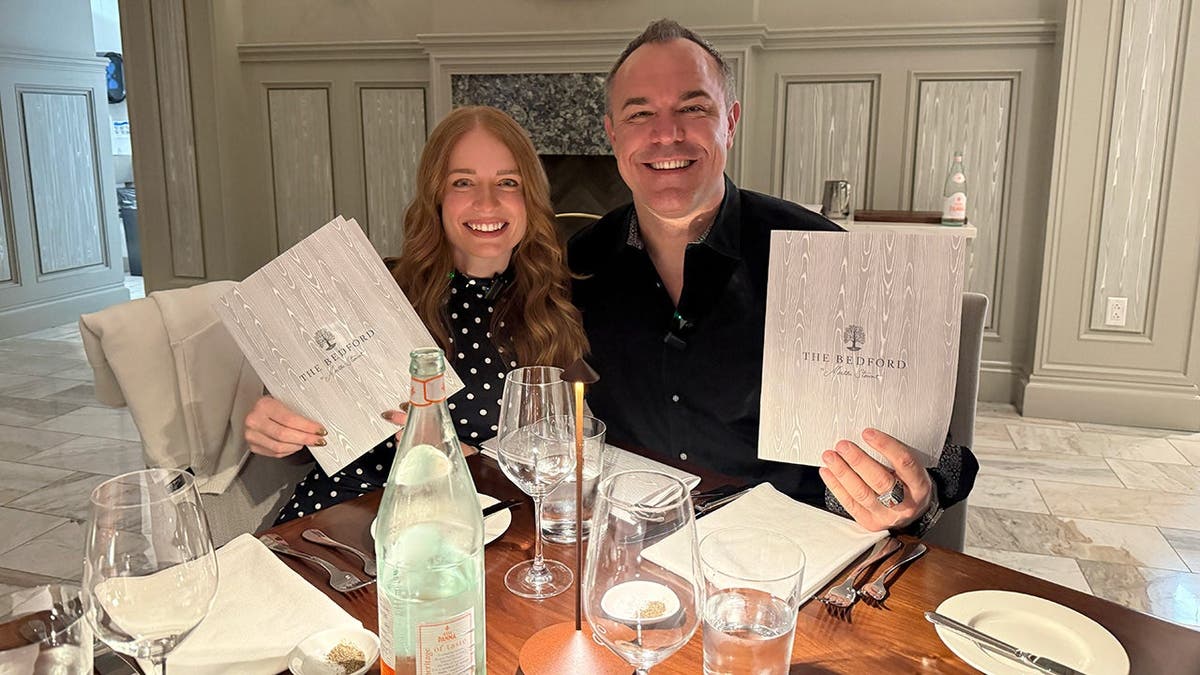 A woman and a man sit at a restaurant and hold menus showing they are at The Bedford by Martha Stewart.