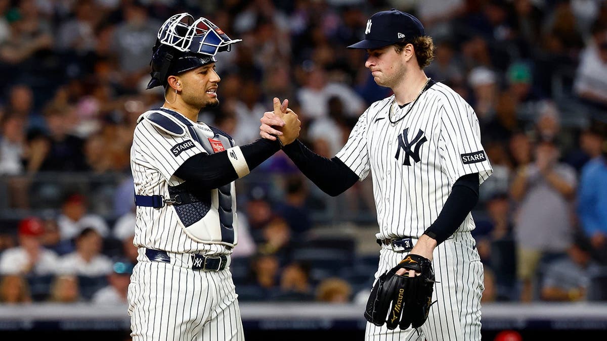 New York Yankees catcher J.C. Escarra and pitcher Cam Schlittler shaking hands on baseball field.