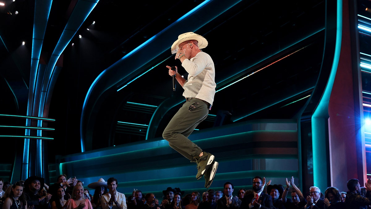 Photo of Kenny Chesney mid-air as he jumps on stage during a performance