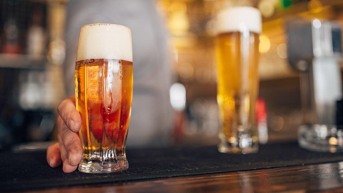 Um homem segura uma cerveja em um bar.