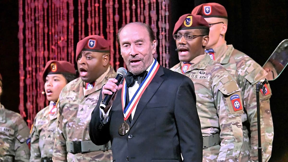 Lee Greenwood sings in front of some service members.