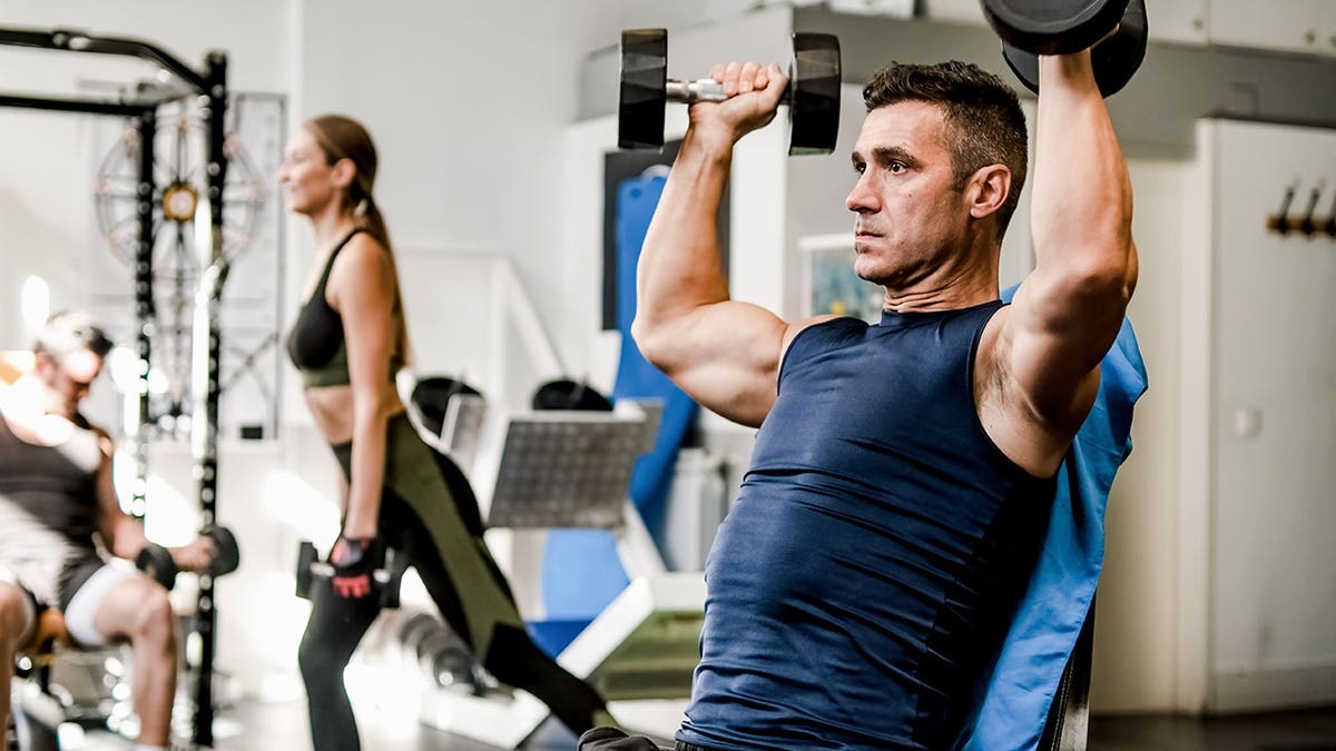 Muscular young male athlete lifting heavy dumbbells in gym