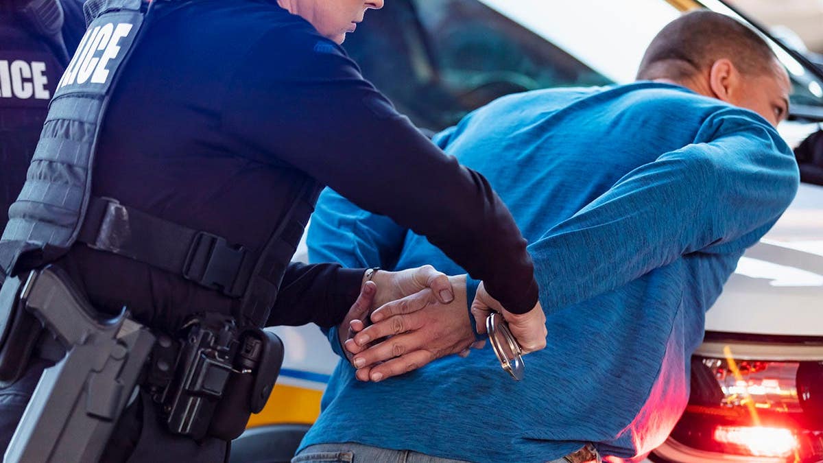 Policewoman and African-American partner handcuffing a man leaning on police car hood