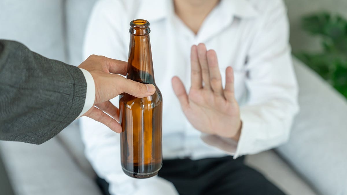 Man refusing to drink whiskey by showing a stopping hand sign.
