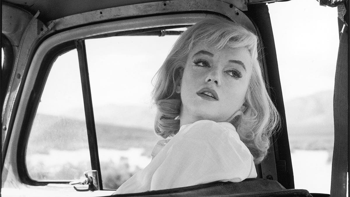 American actress Marilyn Monroe glances over her shoulder from the front seat of a car.