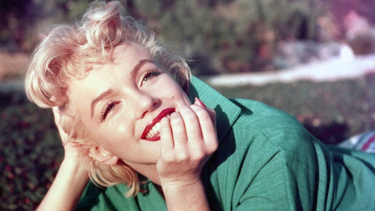 Actress Marilyn Monroe posing lying on grass outdoors.