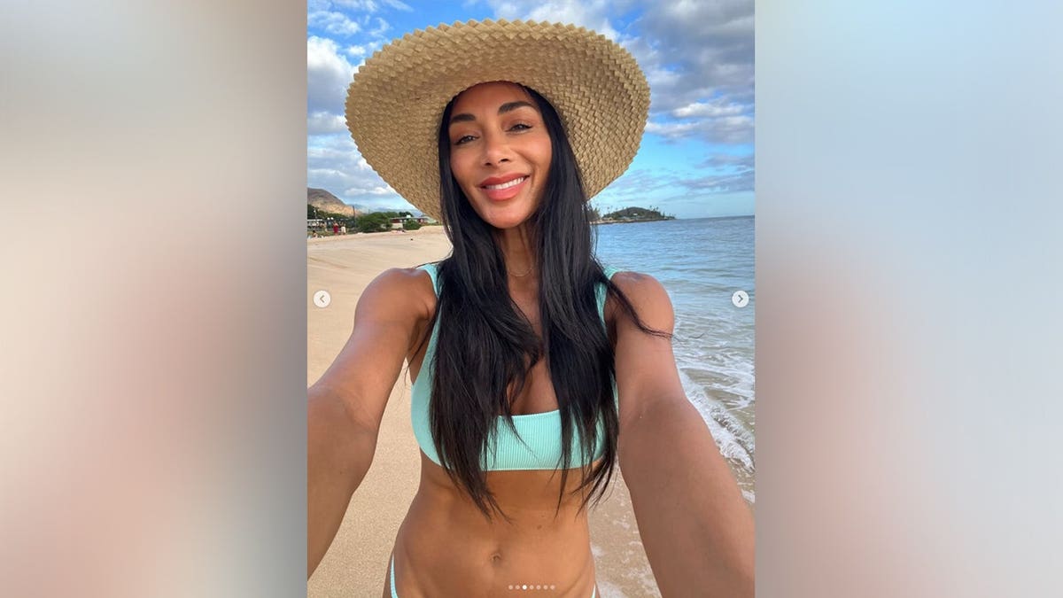 Nicole Scherzinger standing in front of the ocean in a blue bikini