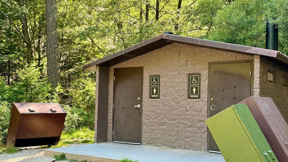 Outhouse with two brown doors and trash bins in a forest setting