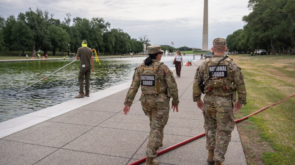 Unos miembros de la Guardia Nacional pasan junto a un empleado del Servicio de Parques Nacionales que está limpiando con una aspiradora el estanque reflectante del Monumento a Lincoln, el viernes 19 de junio de 2026, en Washington.