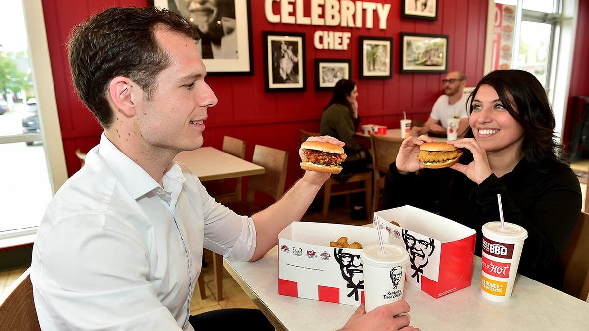 A man and a woman eat KFC sandwiches at a KFC restaurant.