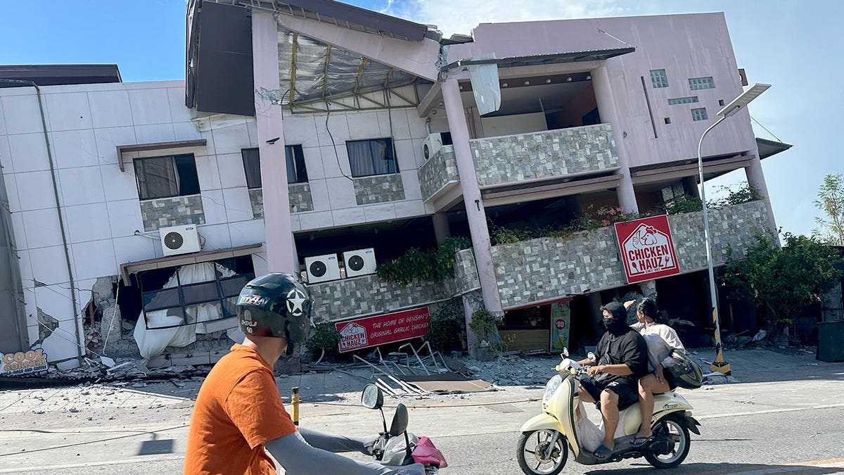 Bikers ride past a collapsing building.