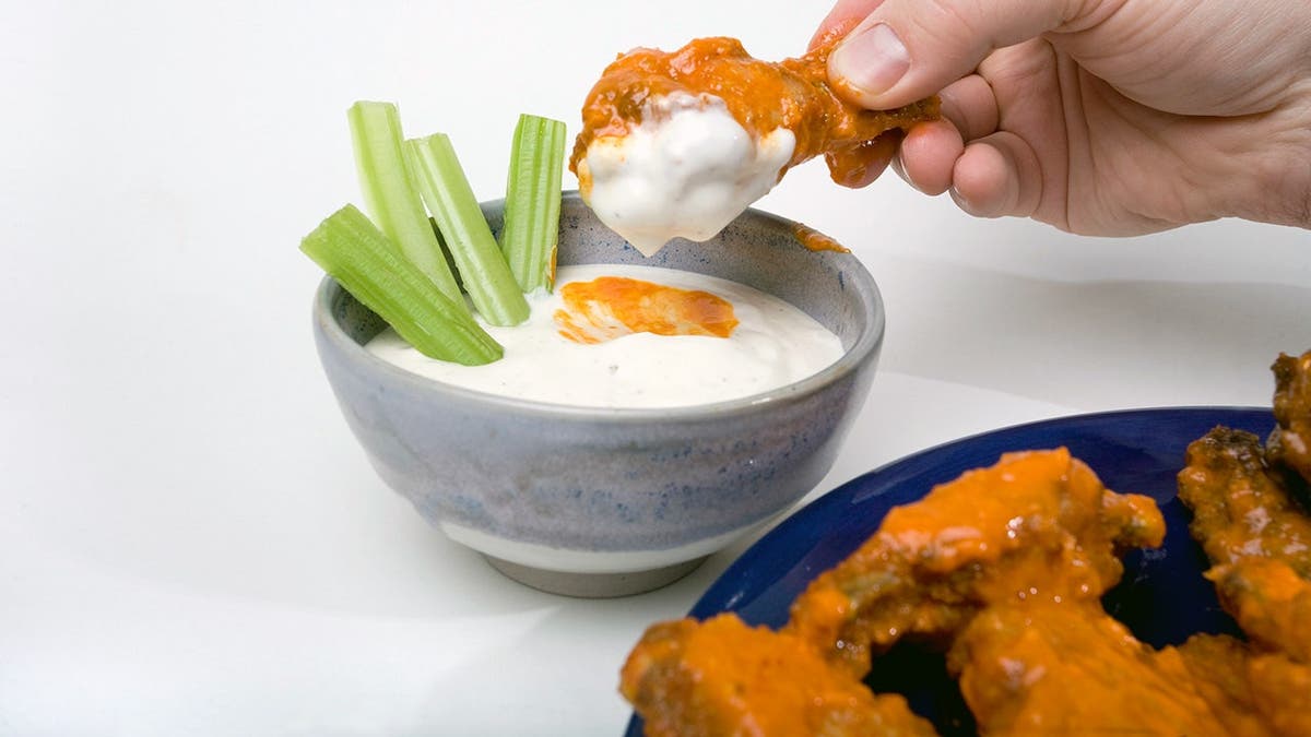 Hand dipping a wing into ranch dressing