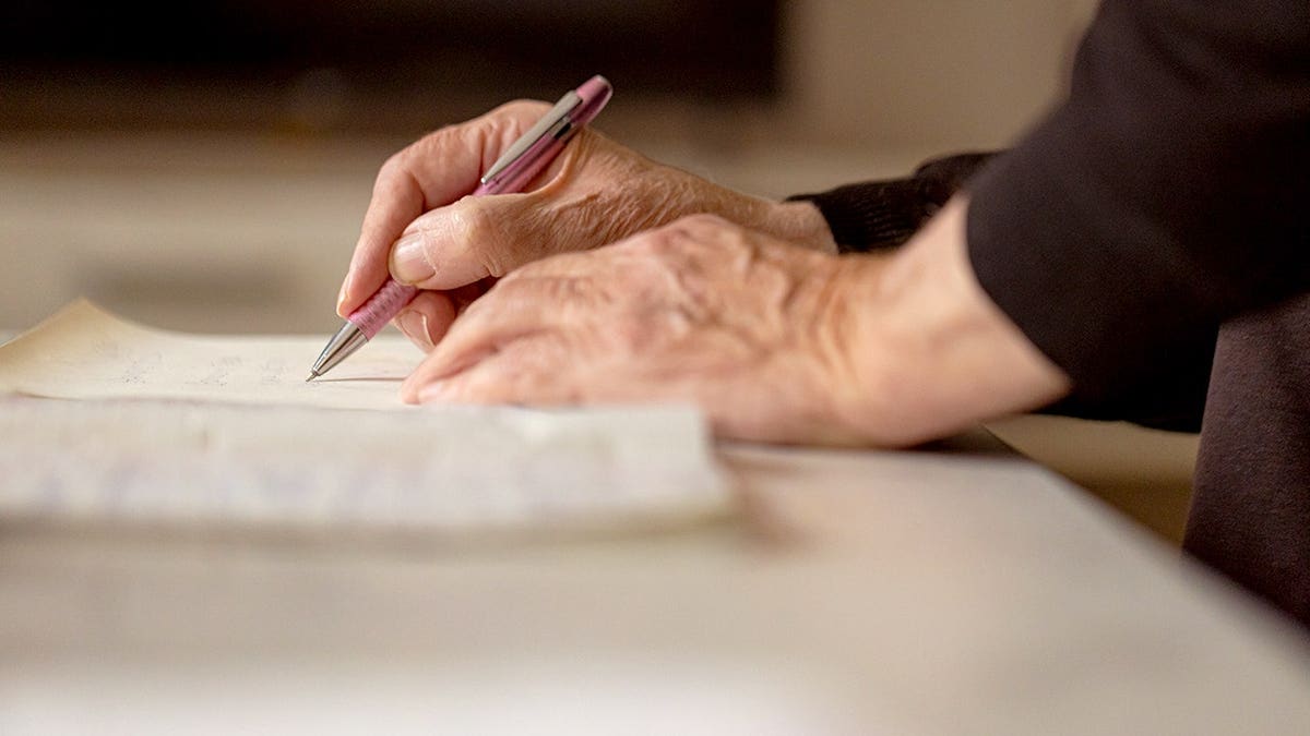 An old man writes in an old notebook with a pen.