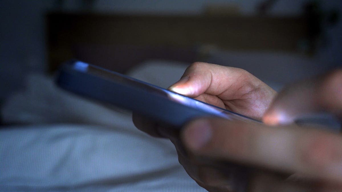 Manos sosteniendo y usando un smartphone en la cama por la noche