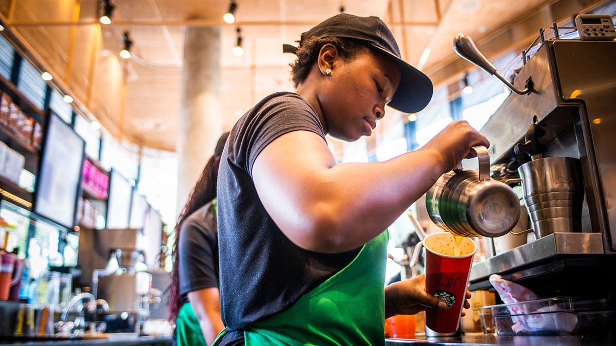 A Starbucks barista pours a drink.