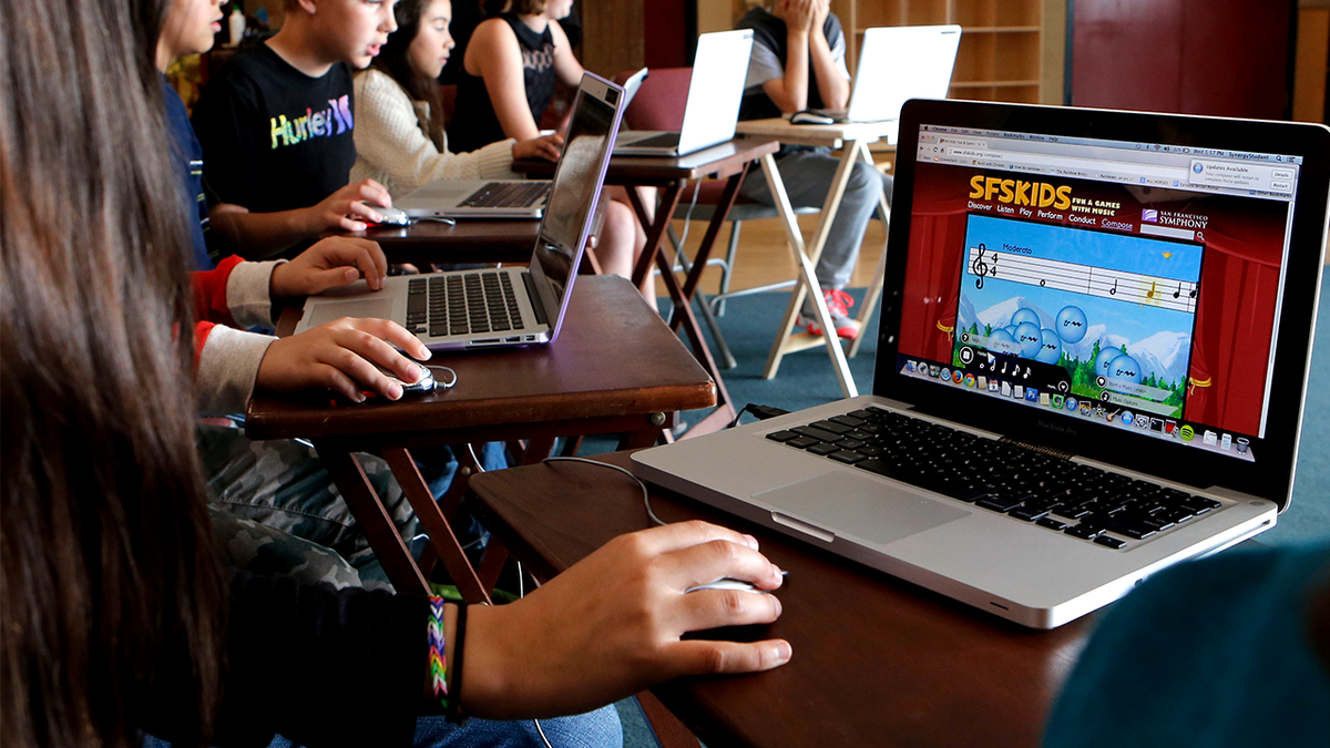 students sit typing laptops in classroom