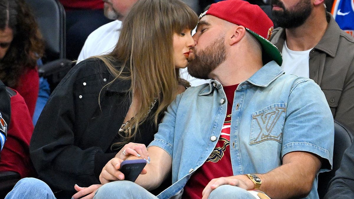 Taylor Swift kisses Travis Kelce at a basketball game.