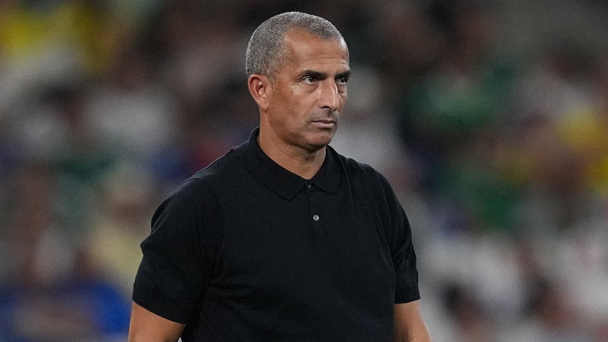 Tunisia head coach Sabri Lamouchi watching soccer match on sidelines.