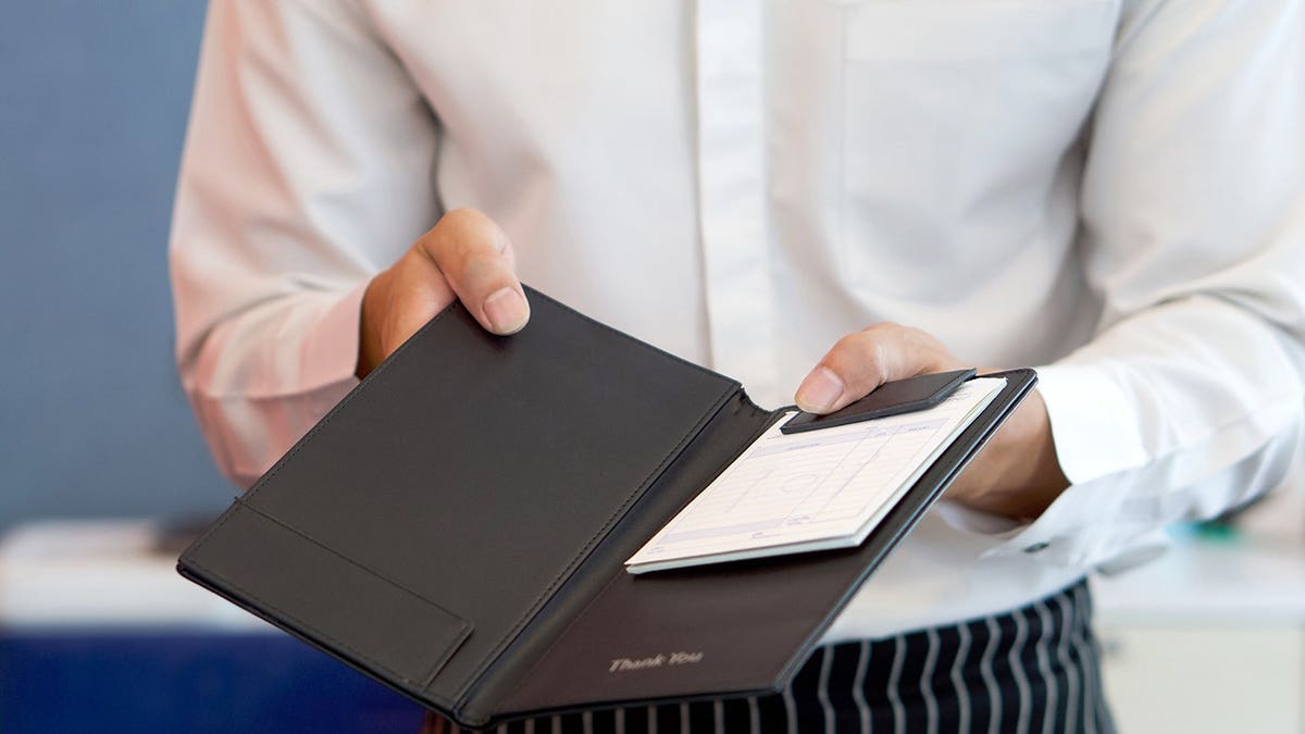 A waiter in a white shirt and apron holding a receipt.