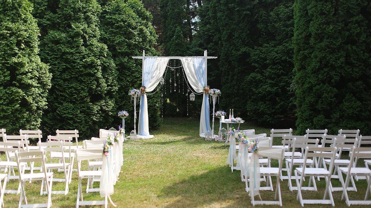 White wedding arch and decorated chairs set up in a park.