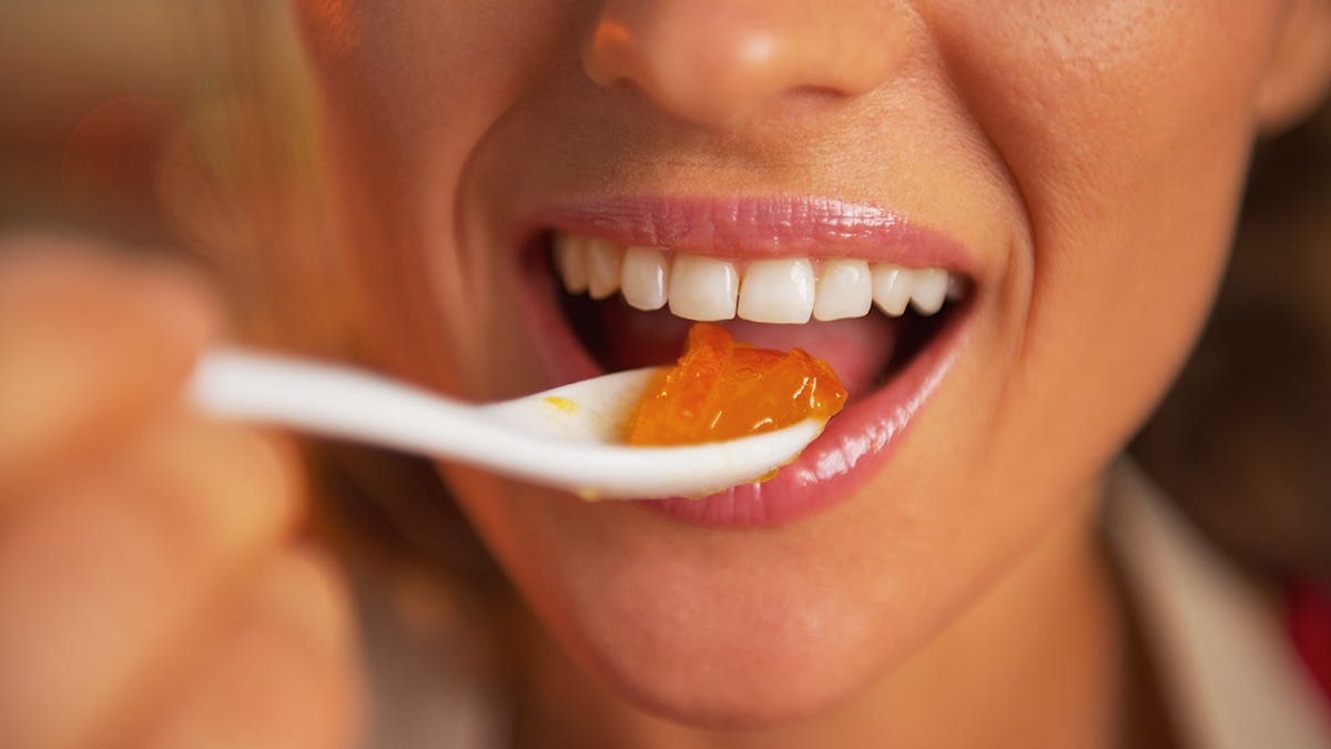 A happy young woman eating orange jam closeup
