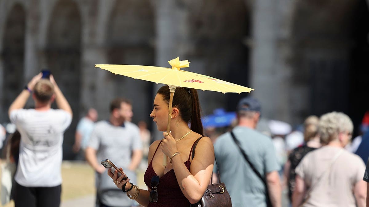 A woman shielding herself with a parasol while walking near the Colosseum in Rome