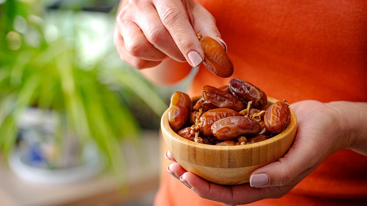 A woman holds a bowl of dates.