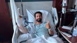 Daniel Crago laying in a hospital bed with his thumb up.