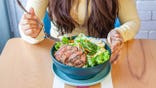 Girl wearing yellow clothes eating a steak and mixed green salad in a cafe.