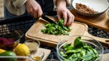 A woman chops spinach on a cutting board.