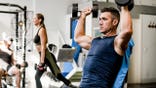 Muscular young male athlete lifting heavy dumbbells in gym