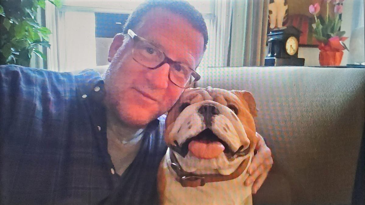 man wearing glasses poses next to a bulldog plushie
