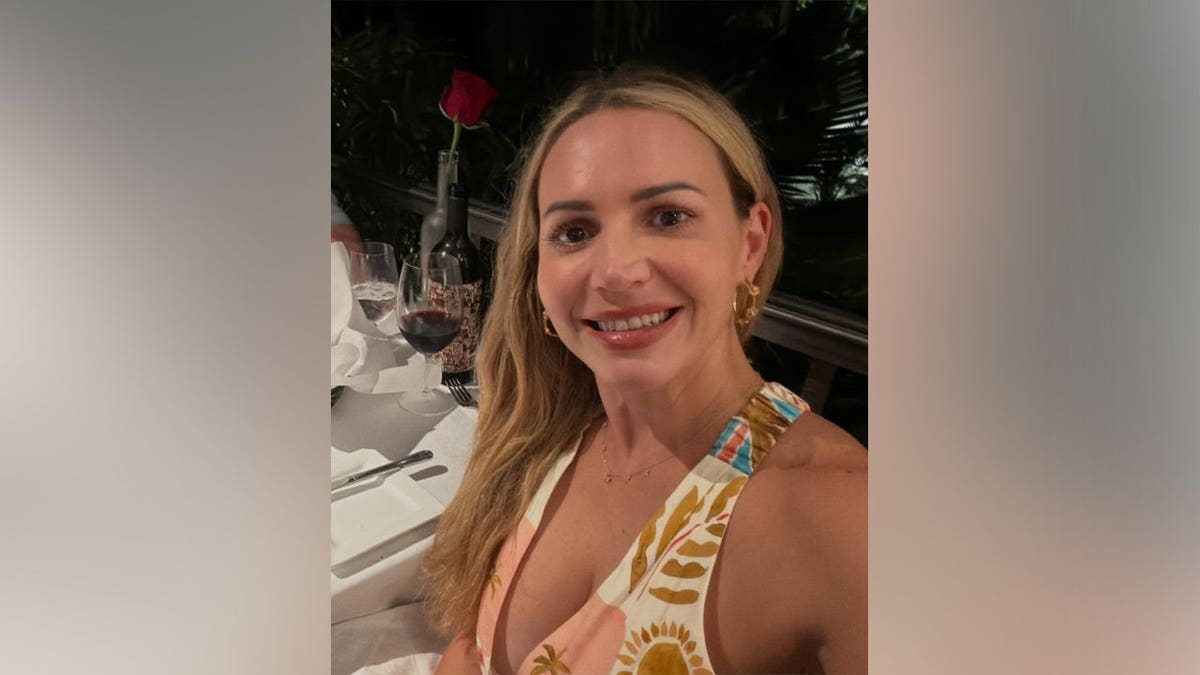 Judge Ashlee Cole smiles while seated at a restaurant table with a glass of red wine and a rose in front of her.