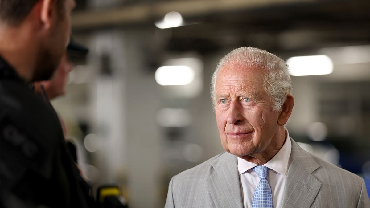 King Charles listening intently in a grey suit.