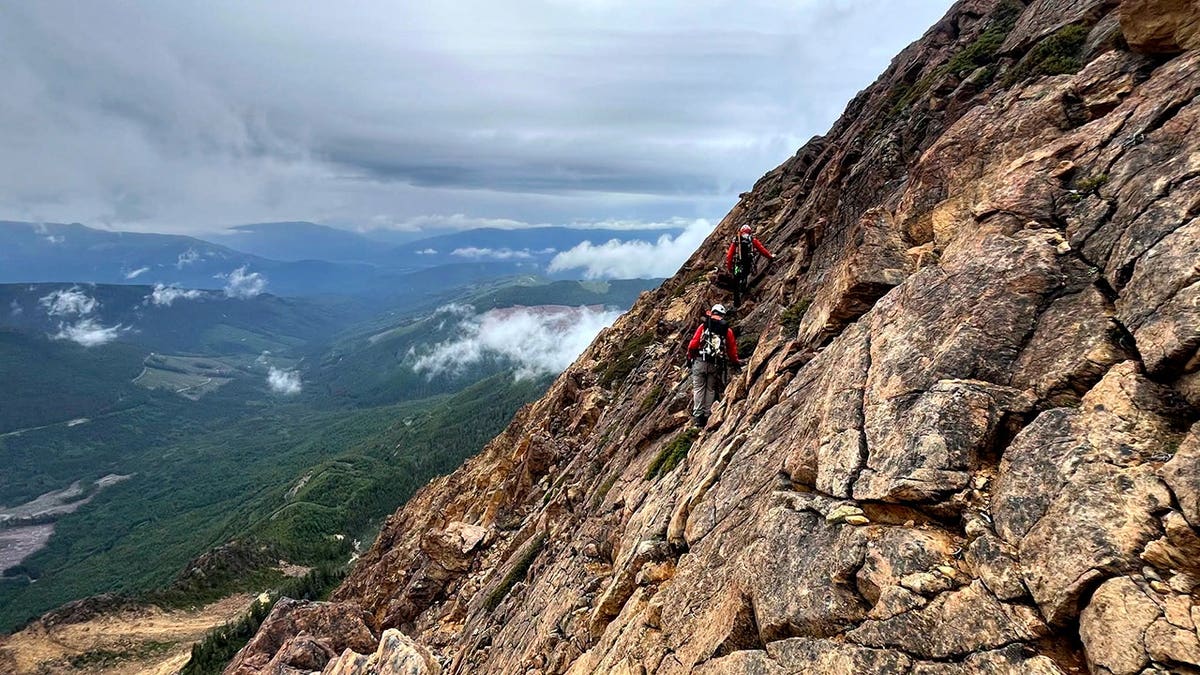 pair of mountain rescue team personnel scaling mountain side