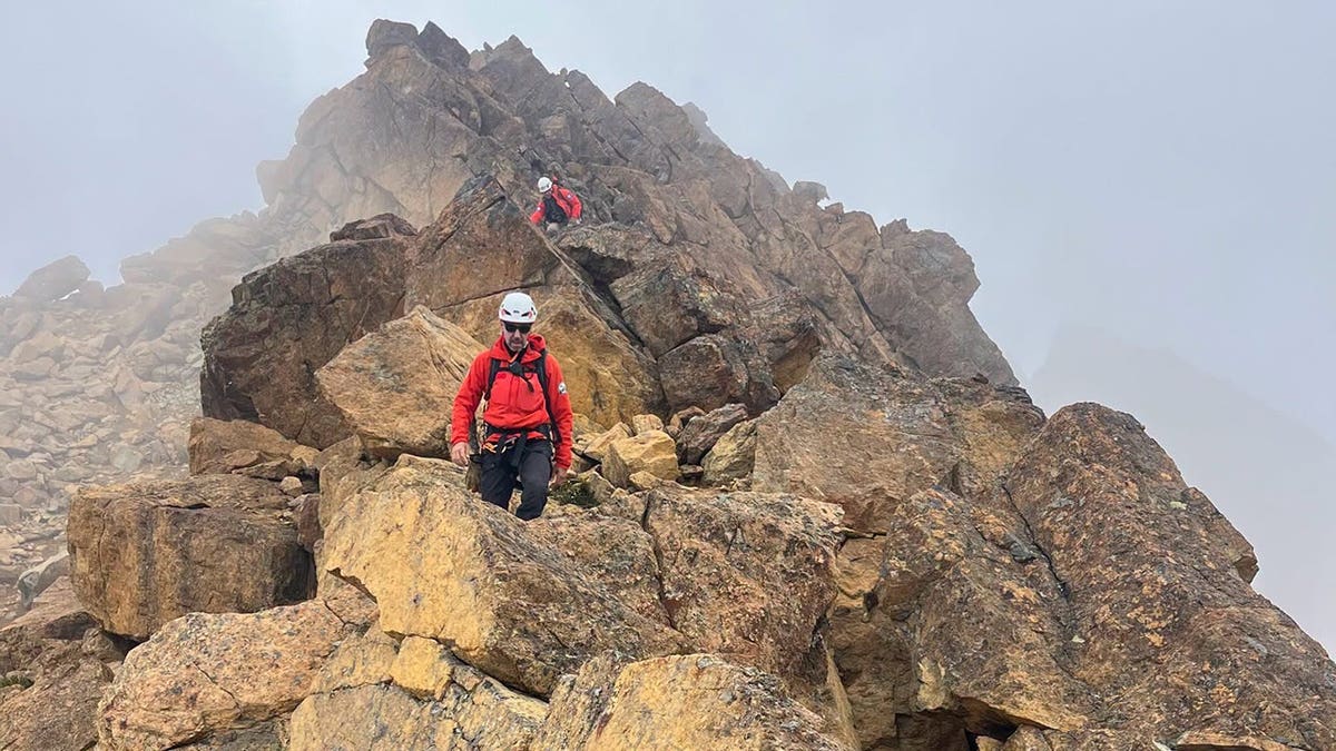 rescue team personnel walking along mountain ridge in foggy conditions