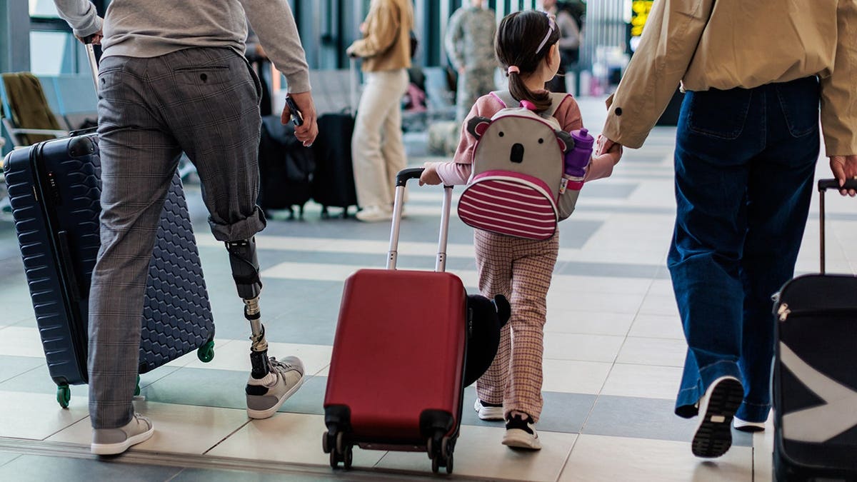 Family walks through airport terminal with luggage.