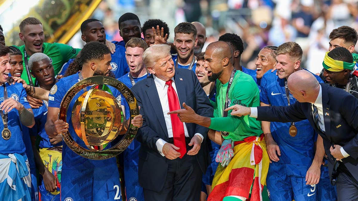 Reece James lifts the FIFA Club World Cup trophy on stage with Donald Trump nearby.
