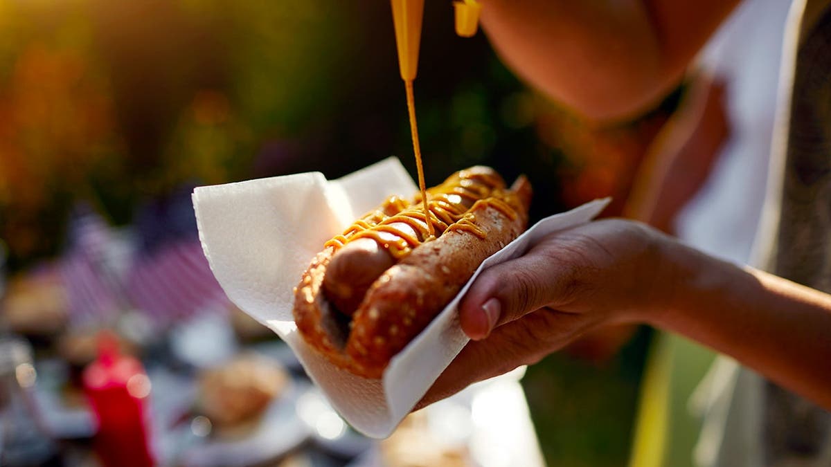 A person puts mustard on a hot dog.
