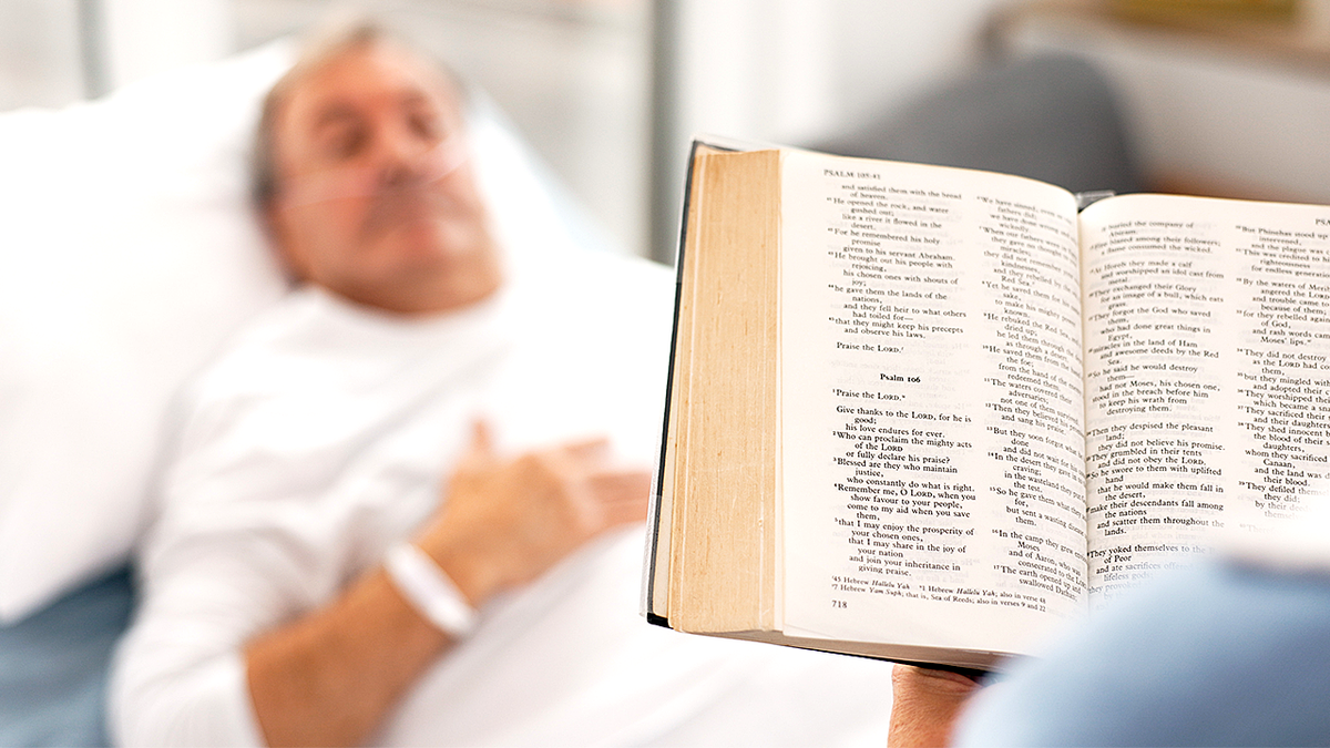 Patient in hospital being read to from a Bible