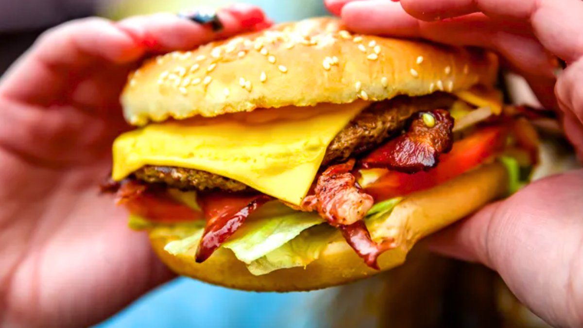 Se ve a una persona con una hamburguesa con queso en la mano.