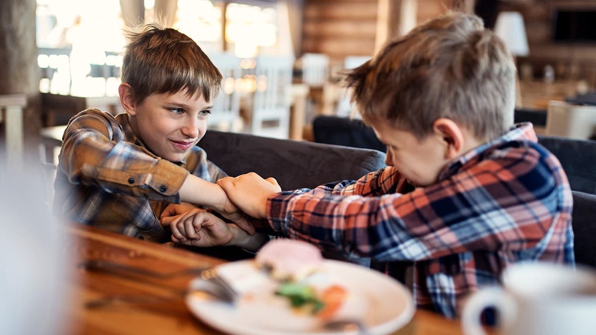 Two boys arm-wrestle at a restaurant.