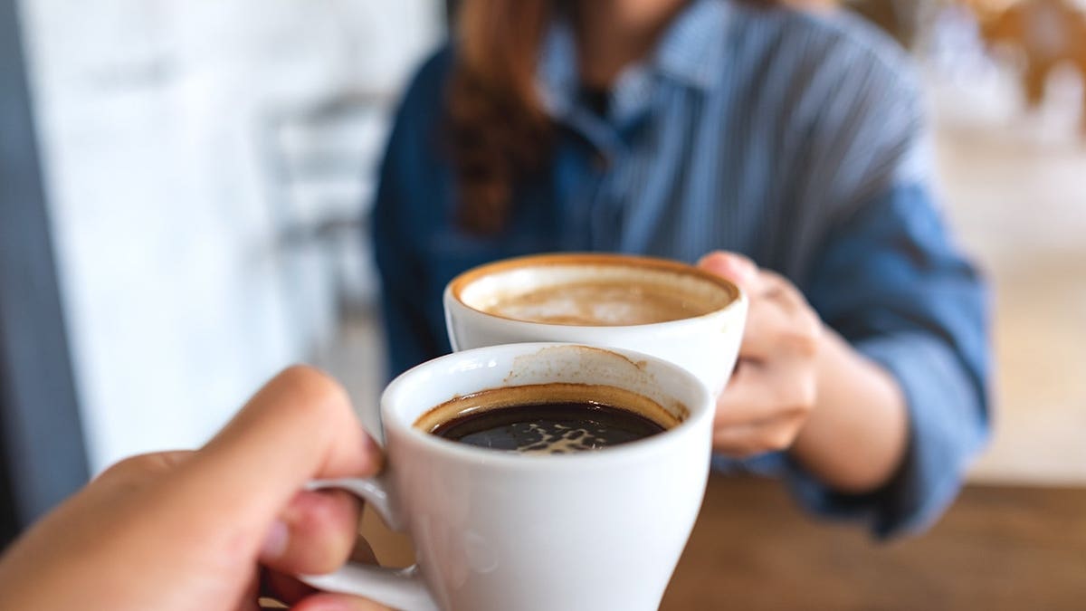 Closeup image of a woman and a man clinking coffee cups together in cafe