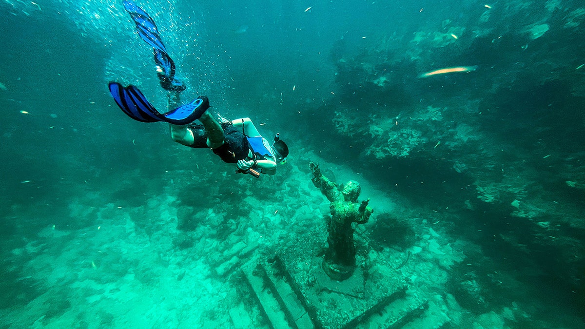 A diver swims adjacent   a submerged statue of Christ successful  the ocean