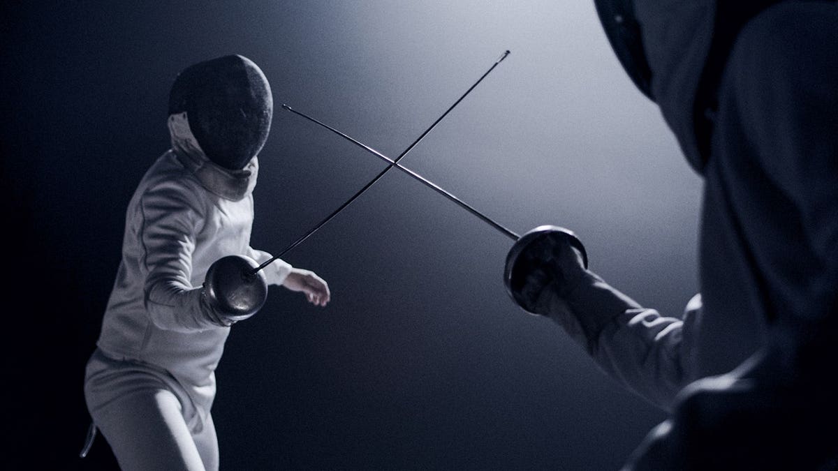 Two fencers dueling with foil swords on a lit stage with blue lighting and smoke effects.
