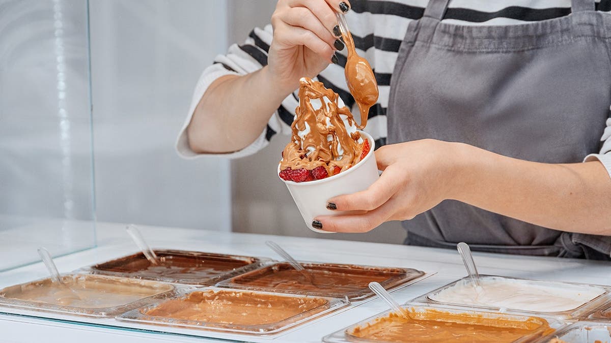 A woman adds toppings to a dish of frozen yogurt.