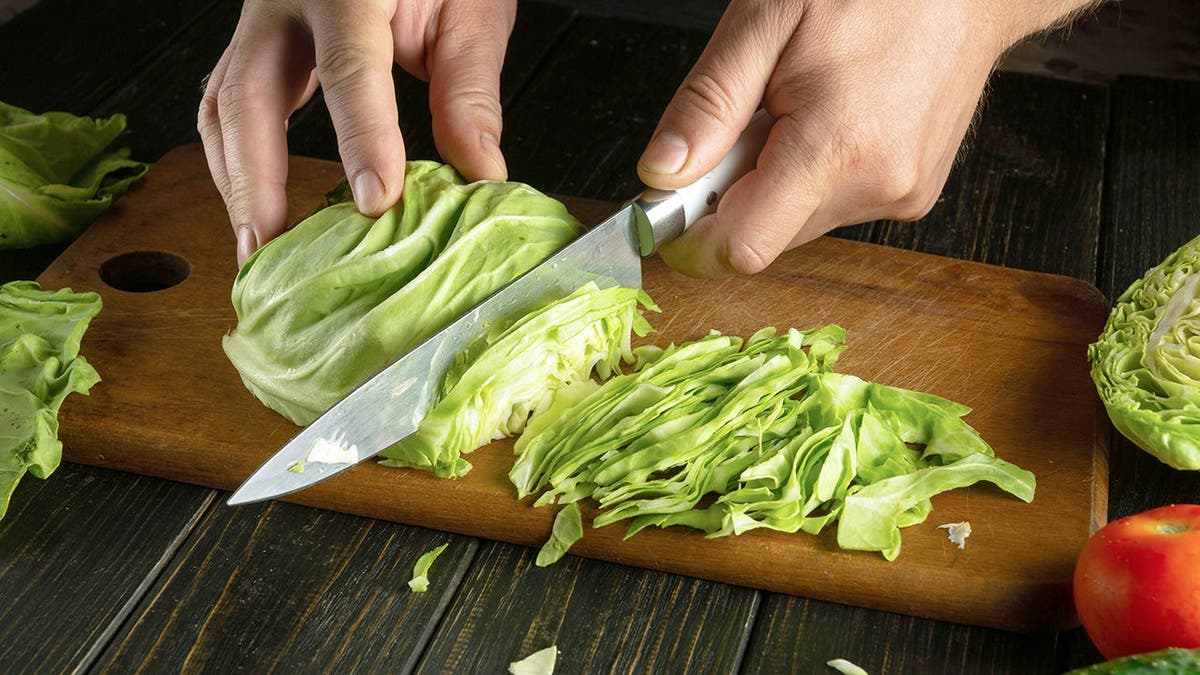A person chops iceberg lettuce on a cutting board.