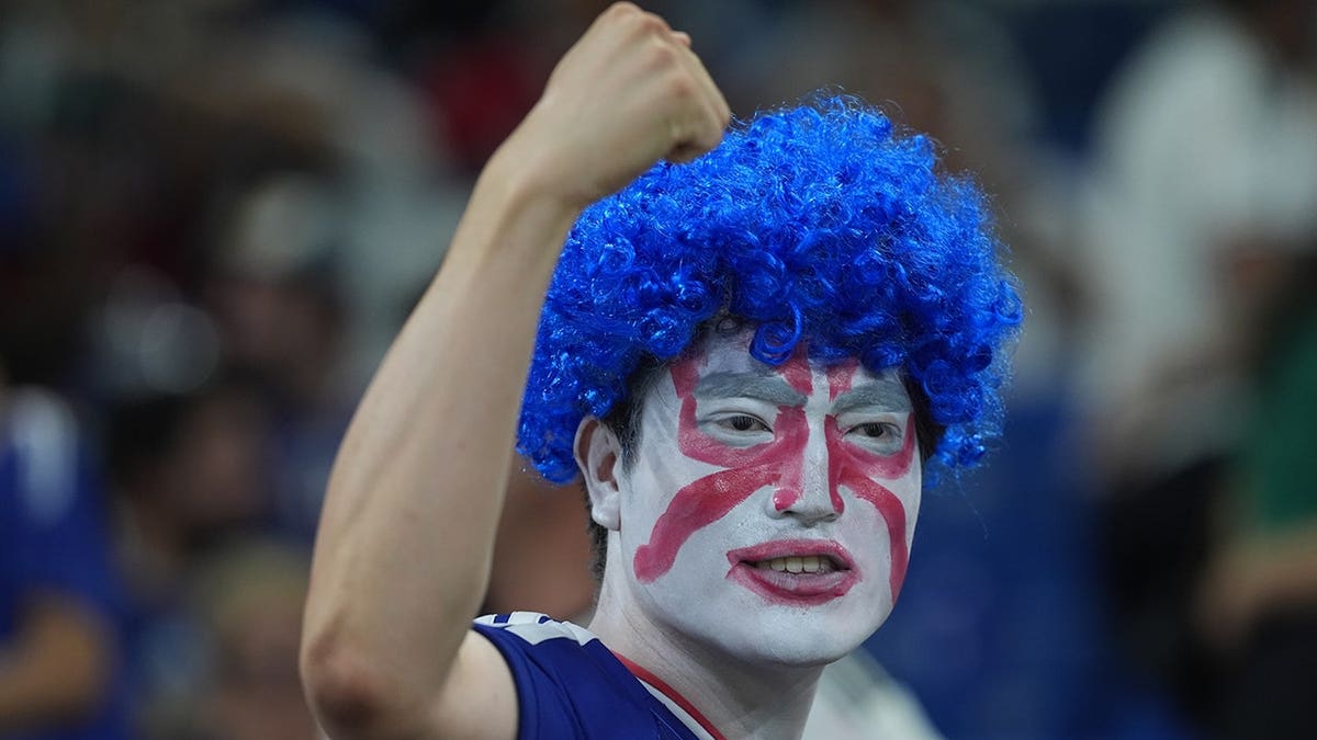 Japan fan fist pumping the air with a bright blue wig on.