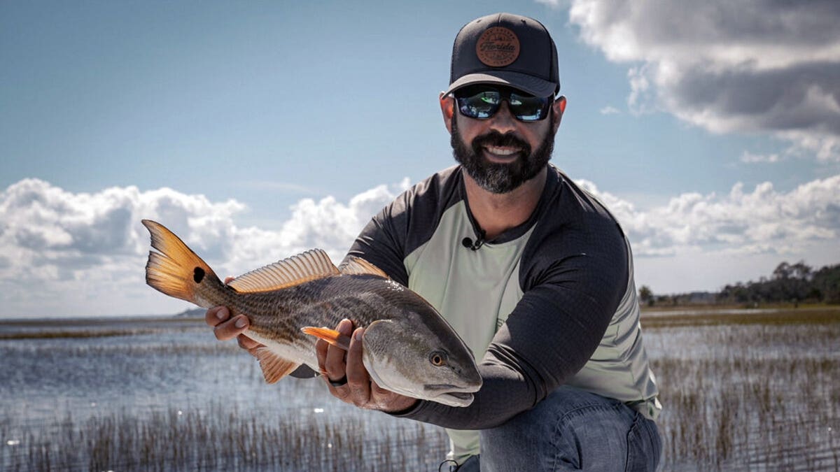 man in a marsh holds up a fish