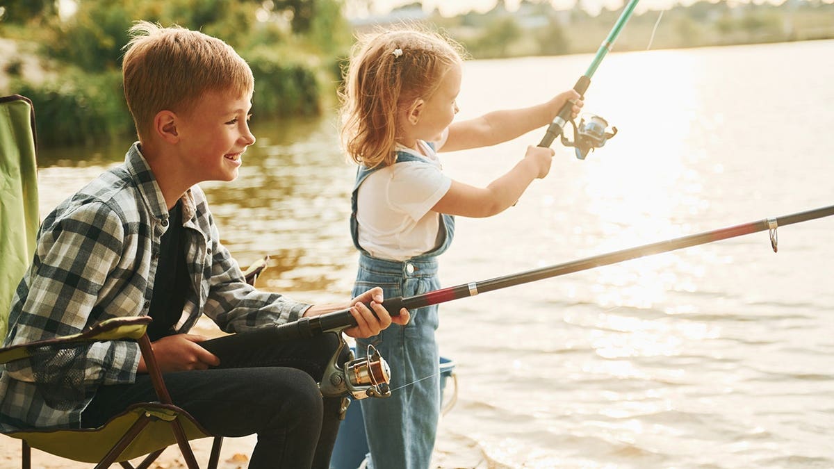 Boy and his sister fish outdoors by a lake